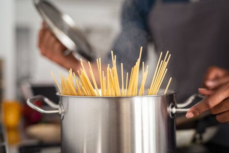 Closeup of spaghetti in pot on stove. Woman holding pot with spaghetti in hot boiling water. Spaghetti ready to be cooked at home.の写真素材