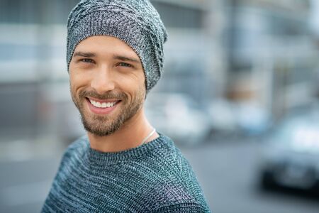 Portrait of smiling man wearing woolen cap outdoor. Handsome young man in winter clothes looking at camera. Closeup face of cheerful guy wearing sweater in winter with copy space.の写真素材