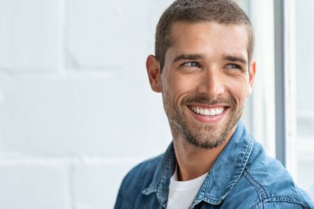 Confident young man looking away with big smile. Happy handsome guy looking through window thinking about the future. Closeup face of smiling casual man imagine with copy space.の写真素材