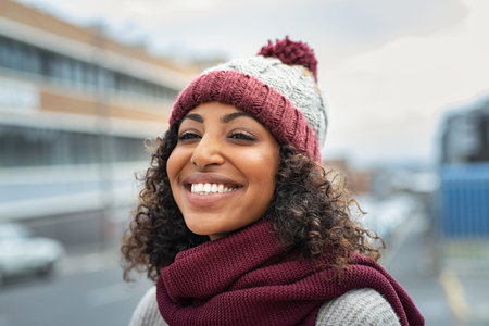 Closeup face of young happy woman enjoy winter, wearing scarf and woolen cap. Smiling black girl...