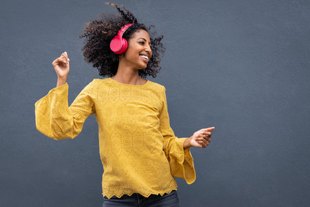 Beautiful black girl listening music in headphones from smart phone or mp3 player and dancing....