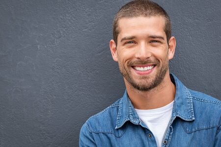 Closeup portrait of a happy young man smiling on gray background. Handsome casual guy with beard looking at camera. Portrait of a cheerful stylish man isolated against gray wall with copy space.の写真素材