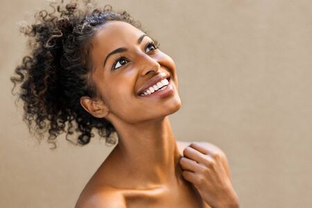 Beautiful african woman laughing and looking up in joy. Portrait of cheerful young woman with bare shoulders isolated on background. Beauty afro american girl with curly hair smiling.の写真素材