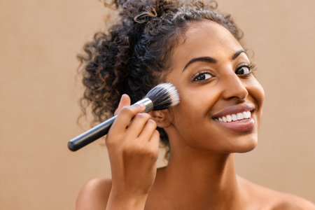 Closeup portrait of african woman applying foundation with makeup brush. Black beauty girl gets...