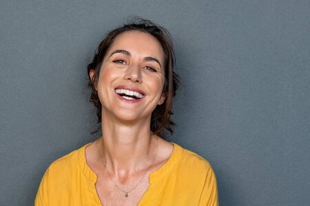Portrait of mature woman laughing against grey background. Successful middle aged woman in casual clothing with toothy smile looking at camera. Cheerful happy young beautiful latin lady smiling with copy space.の写真素材