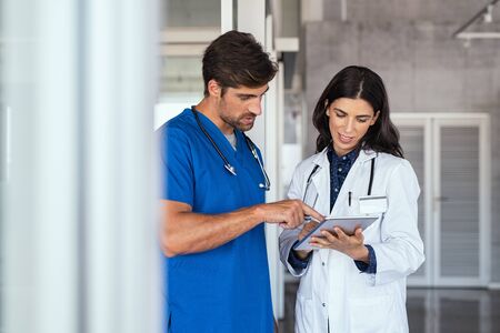 Doctor and nurse discussing over a medical report in hospital. Female mature doctor and nurse checking clinical report of patient online. Healthcare staff having discussion in a hallway of private clinic.の写真素材