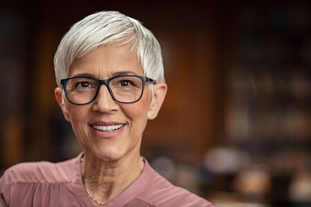 Portrait of beautiful senior woman looking at camera with copy space. Successful mature business woman wearing eyeglasses. Happy old professor in standing in college library with gray hair.の写真素材
