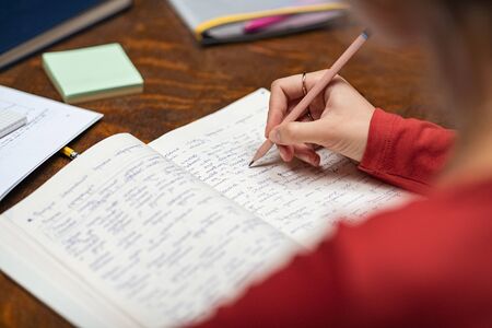 Closeup of woman hand taking notes in notebook. University student studying for exam reading handwritten notes. Young woman hand marking important points in notebook while studying.の写真素材