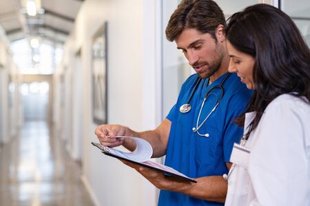 Team of doctors working together on patients file at hospital. Medical staff analyzing report and working at clinic. Woman doctor having discussion in a hospital hallway with nurse, copy space.の写真素材