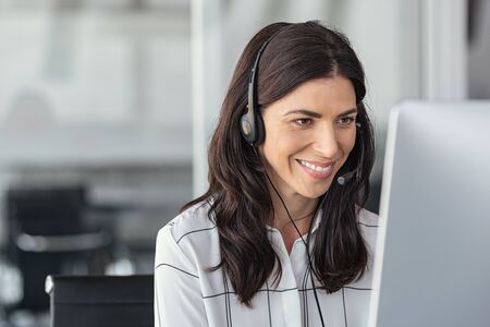 Call center business woman talking on headset. Portrait of mature woman working on computer with headset in office. Smiling friendly telephone operator with headset working on support customer service at office with copy space.の写真素材