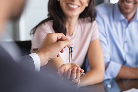 Close up of man hand giving house keys to woman. Smiling mature woman receiving new house keys from real estate agent. Man delivering keys to client for new home. Real estate agent giving keys to apartment owner.の写真素材