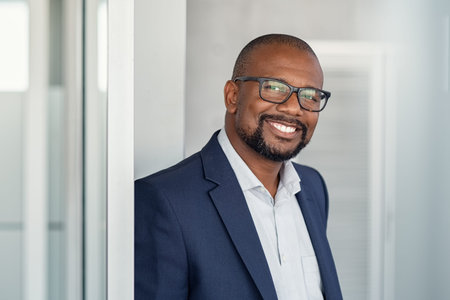 Portrait of happy african man wearing spectacles and looking at camera. Successful black buinessman with beard and glasses feeling confident at work. Portrait of mature business man in formalwear smiling.Â の写真素材
