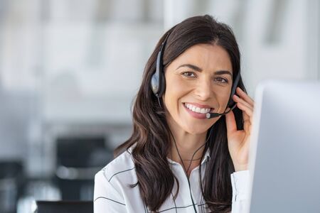 Call center agent with headset working on support hotline in modern office with copy space. Portrait of mature positive agent in conversation with customer over headset looking at camera. Consulting and assistance service customer support.の写真素材