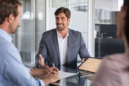 Confident financial agent showing growth graph to couple. Mid couple meeting financial advisor for investment. Business people discussing the charts and graphs showing the results of their successful teamwork.の写真素材