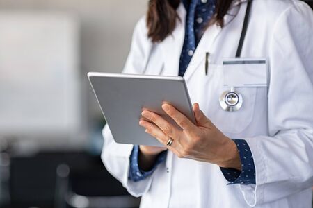 Close up of woman doctor hands using digital tablet at clinic. Closeup of female doctor in labcoat and stethoscope holding digital tablet, reading patient report. Hands holding medical report, copy space.の写真素材