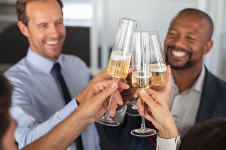 Business people raising toast with champagne at modern office. Smiling team of business people clinking their flutes of white wine in a meeting room. Successful business man raising glasses of champagne in the office.の写真素材