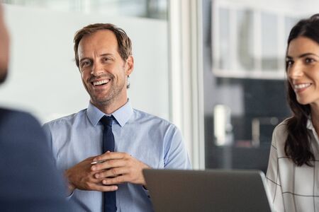 Business partners discussing ideas at meeting. Successful businessman and woman listening to colleague during meeting in modern office. Cheerful mature business man and businesswoman smiling during brainstorming.の写真素材