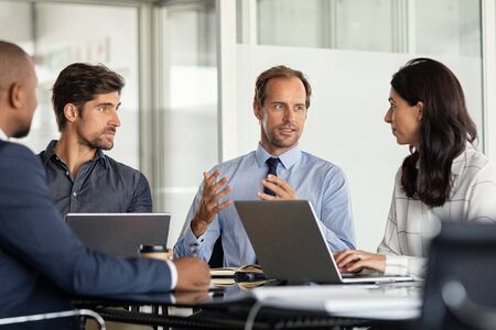 Businessman giving some new ideas about project to his partners in conference room. Mature leader discussing over new business plans in office with his employees. A group of businessmen and businesswoman talking during meeting.の写真素材