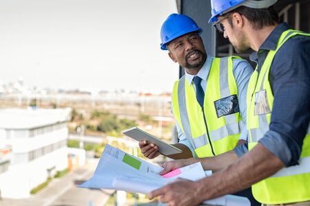 Construction workers talking about new construction site with copy space. Engineers in mechanical factory reading instructions. Architect in construction uniform holding blueprint and discussing. の写真素材