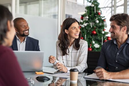 Group of happy business people in meeting during christmas holiday. Smiling businessman and businesswoman discussing new project strategy during xmas time. Successful multiethnic business partners in a conversation in modern office.の写真素材