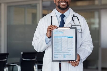 Successful doctor holding hospital admission form attached on clipboard. Close up of african doctor holding clipboard with form at hospital. Nurse showing blank medical information document for registration at private clinic. の写真素材