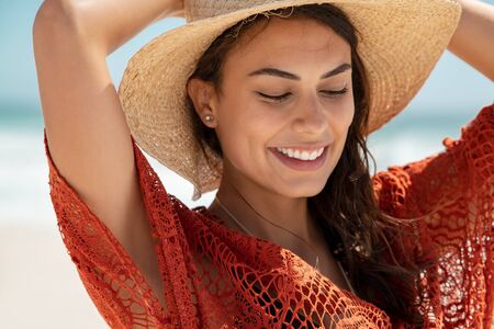 Carefree young woman at beach enjoying summer holiday. Portrait of happy smiling hispanic woman relaxing at sea during vacation. Close up face of beautiful fashion girl with red crochet dress walking on the beach.の写真素材