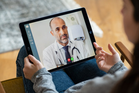 Back view of young woman making video call with her doctor while staying at home. Close up of...