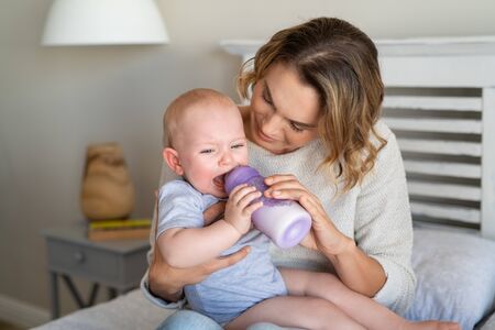 Mother holding and feeding hungry baby from milk bottle. Portrait of crying newborn baby being fed by his mom using bottle. Loving woman giving to drink milk to her crying son.の写真素材