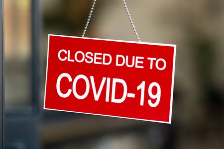 Temporarily closed sign for Coronavirus in small business activity. Information notice sign about quarantine measures in a restaurant. Close up on a red closed placard in the window of a shop displaying the message Closed due to Covid-19.の写真素材