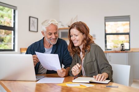 Mature smiling couple sitting and managing expenses at home. Happy senior man and mid woman paying bills and managing budget. Middle aged couple checking accountancy and bills while looking at receipt.の写真素材