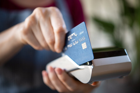 Close up hands of waitress holding credit card machine terminal and swiping debit card to pay the...