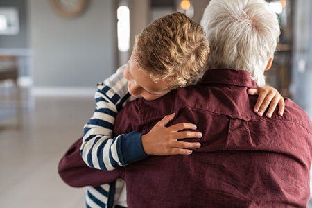 Back view of senior man embracing little boy at home. Lovely grandson hugging old granddad at home....