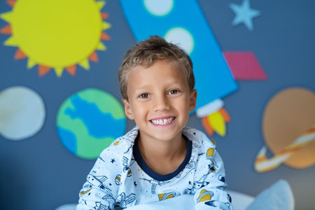 Portrait of smiling boy sitting in space decorated bedroom  the solar system and planets made of...