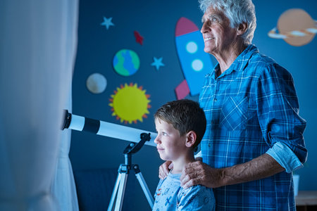Smiling old man and little boy standing near window near a telescope to watch the galaxy.