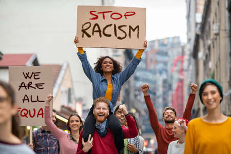 Young group of men and smiling women marching through the city during a Black Lives Matter protest. Group of multiethnic people on city street holding cardboard against racism during a protest. People protesting on road for equality and justice.の写真素材