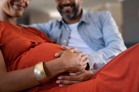 Close up of indian man feeling pregnant woman stomach. Smiling mid adult couple expecting child while father touching baby bump. Close up hands of happy expectant mixed race couple feeling baby movement.の写真素材