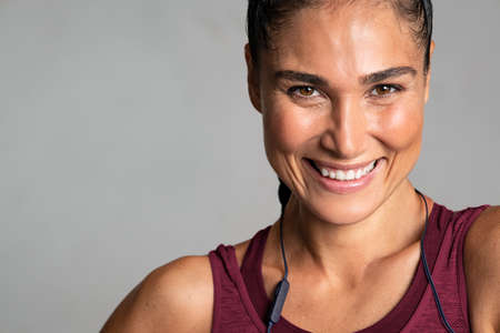 Portrait of beautiful latin woman smiling isolated on grey background. Close up face of sporty woman with big grin looking at camera on gray wall with copy space. Happy fit mixed race girl in sportswear laughing.の写真素材