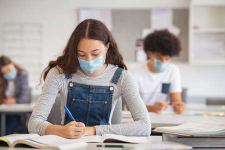 High school student taking notes from book while wearing face mask due to  emergency.の写真素材