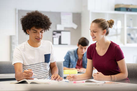 High school students working together on project in classroom. Young african guy and smiling girl preparing for exam by studying together in university library. Two multiethnic college students doing homework together in class.の写真素材