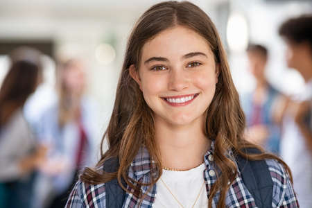 Portrait of beautiful girl standing in college campus and looking at camera. University young woman with backpack smiling. Satisfied and proud student girl standing in high school hallway.の写真素材