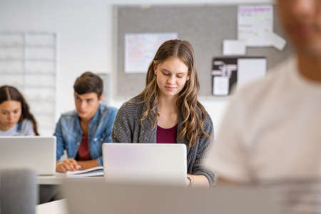 Casual young woman working on laptop in classroom. University students in school working with laptop in library. Group of multiethnic college students in class using laptop.の写真素材