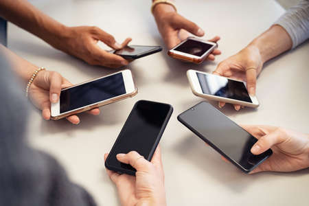 Close up of guys and girls hands in circle using smart phone. High angle view of multiple hands holding mobile phone with empty screen. Group of multi cultural friends using smartphone together, concept of urban youth lifestyle and mobile communication technologies.の写真素材
