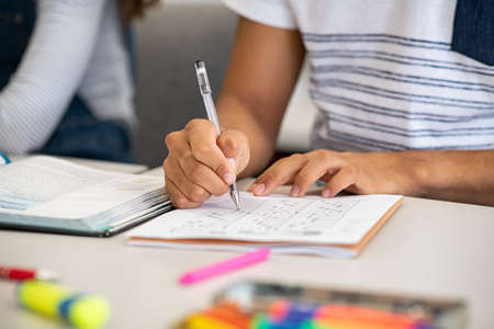 Close up of african student giving exam writing on paper. Closeup of black guy hands holding pen marking answers on examination in college. Student hand fiiling out answers with multiple questions on the test.の写真素材