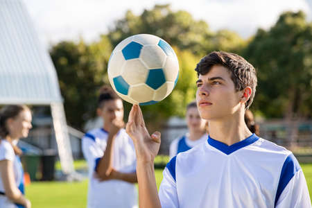 Football guy in uniform spinning football on finger. Handsome soccer player training his skills with a ball. Young man spinning a ball on his finger in playground, copy space.の写真素材