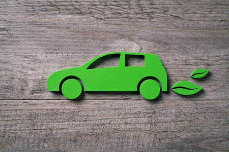 Close up of single green eco-friendly car with leaves silhouette behind. High angle view of wooden cut out of ecofriendly vehicle on wooden table. Concept of green electric car with leaves on plank.の写真素材
