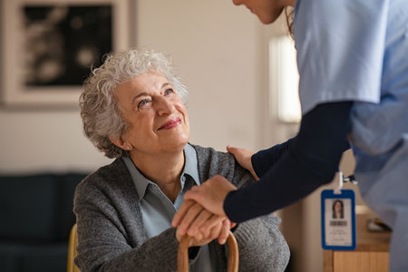 Old woman talking with a female doctor while holding hands at home. Smiling senior woman talking to her general practitioner visiting her at home during virus epidemic. Happy old patient holding hands of caregiver at nursing home.の写真素材
