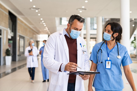 General practitioner and young nurse wearing surgical face mask against covid-19 while having a...