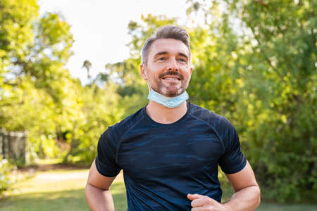 Happy mature man running in park with face mask during  pandemic. Smiling mid adult man jogging outdoor with surgical face mask for safety against covid19 outbreak.の写真素材