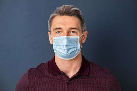 Handsome mature man wearing face mask isolated against grey wall. Smiling positive man wearing surgical mask and looking at camera isolated on gray background.の写真素材