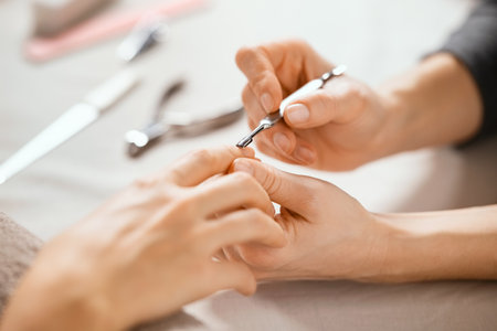 Close up of hands of professional salon worker holding client hand while using cuticle pusher. Process of manicurist using cuticle pusher when working with girl client. Nail technician giving customer a manicure at nail salon.の写真素材